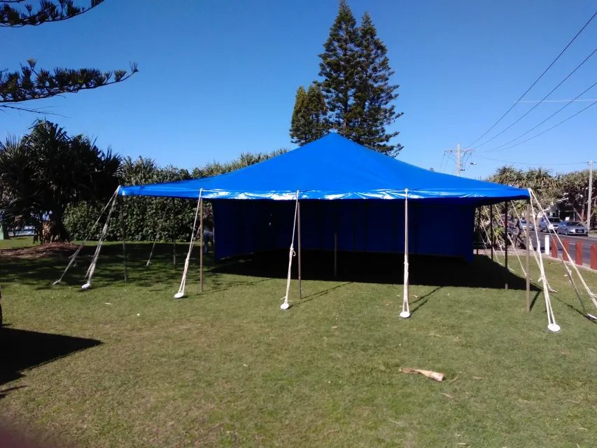 Blue peg-and-pole marquee with walls on a coastal lawn under Norfolk pines