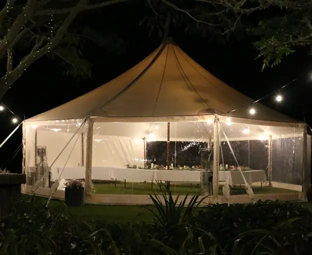 Clear-wall marquee lit at night with long tables set for dinner