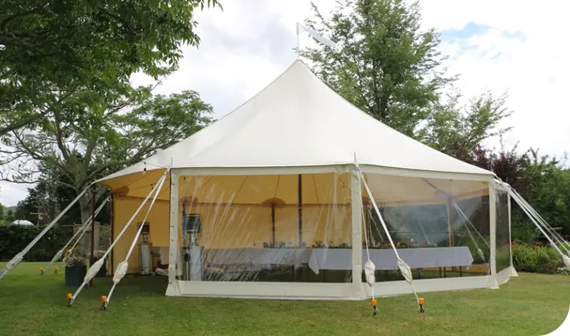 Tables set for a reception inside a marquee with clear walls on a bright day