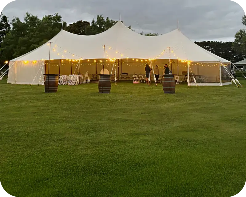 Hampton marquee with sweeping cream roof, festoon lights and wine barrels on a lawn