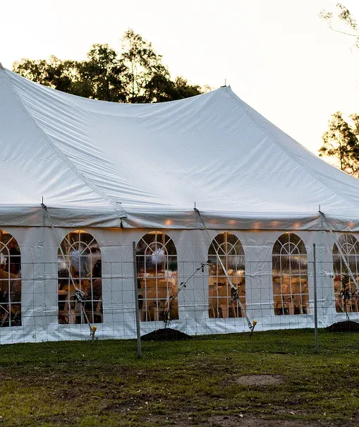 Long 10 m by 21 m peg-and-pole marquee glowing at dusk