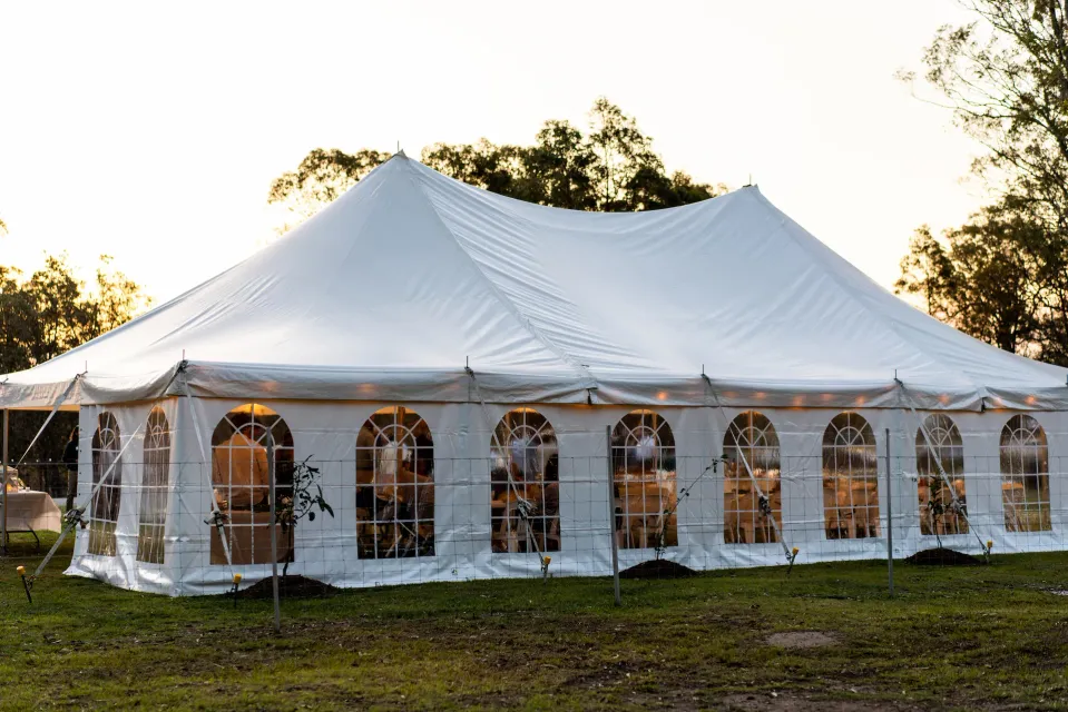 White peg-and-pole marquee with arched clear windows at sunset, guests seated inside