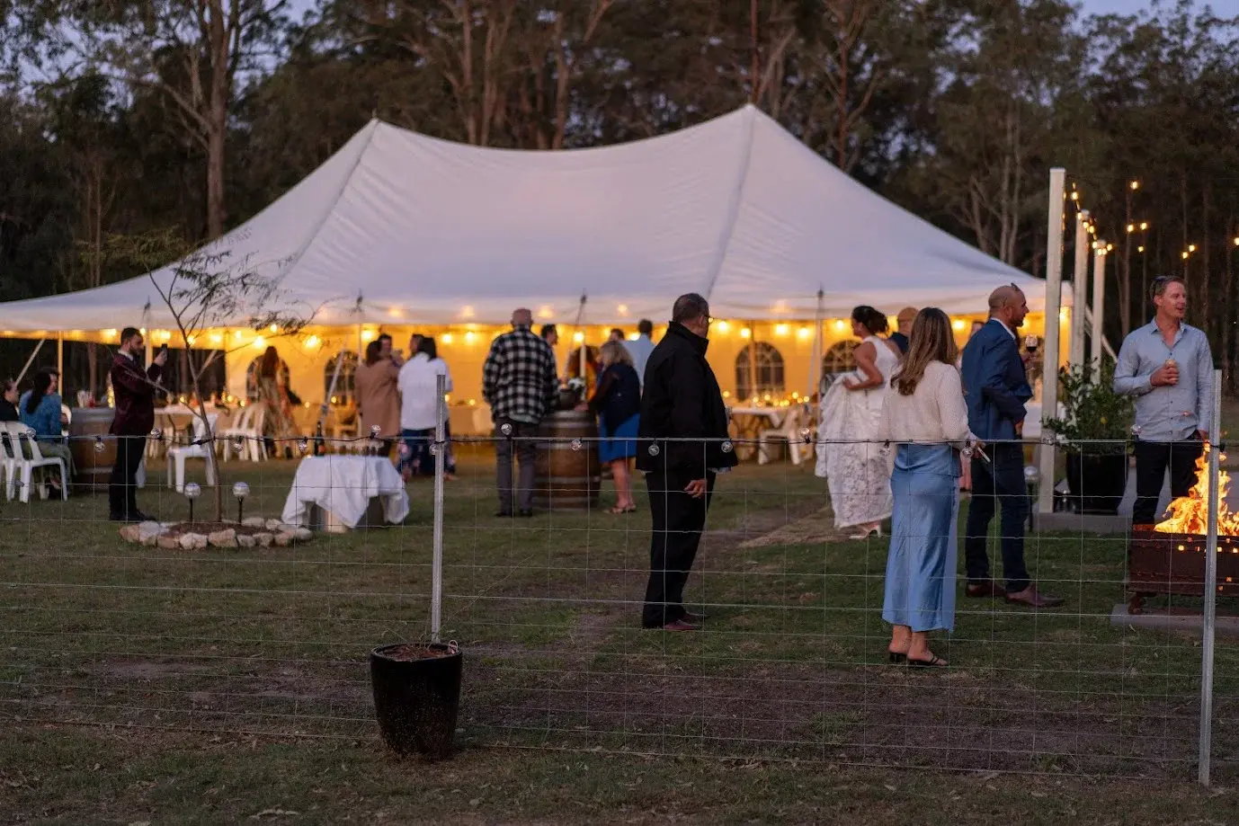 Guests outside a glowing marquee at dusk in bushland