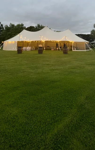 Peg-and-pole marquee on a lawn at dusk with festoon lights