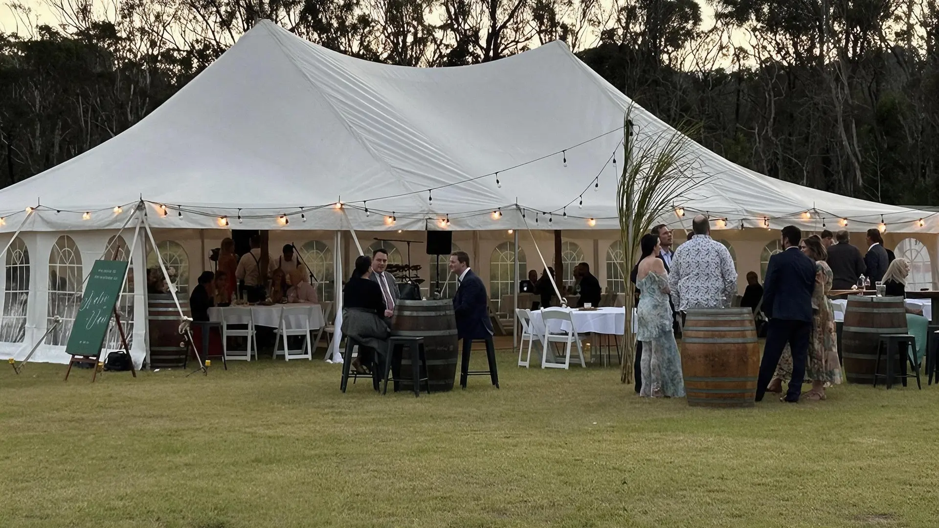 Wedding guests gathered outside a glowing peg-and-pole marquee at dusk in the Clarence Valley
