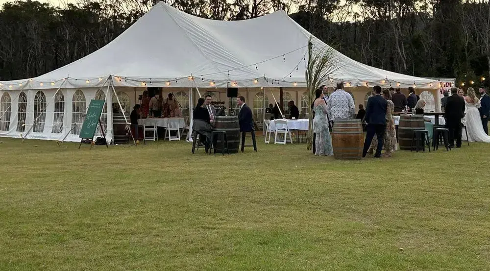 Wedding guests mingling outside a lit peg-and-pole marquee at dusk