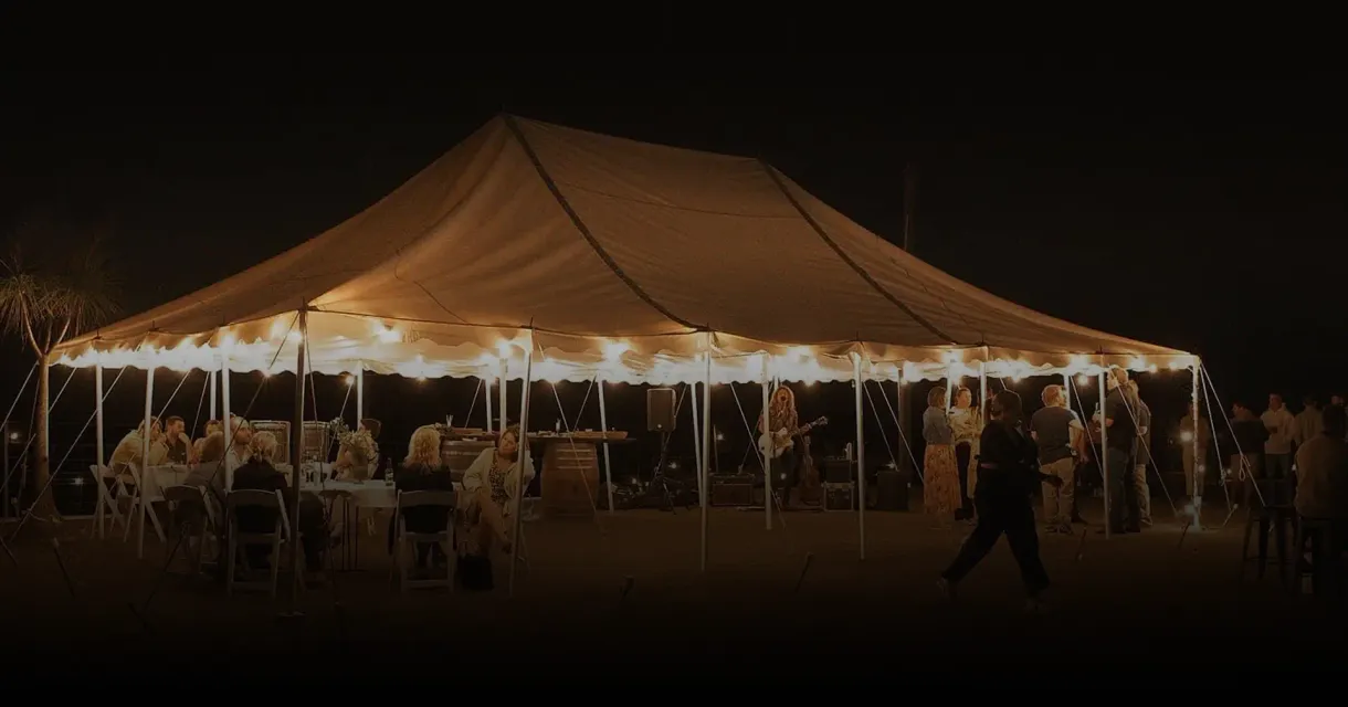Tables set under festoon lights inside a marquee at night