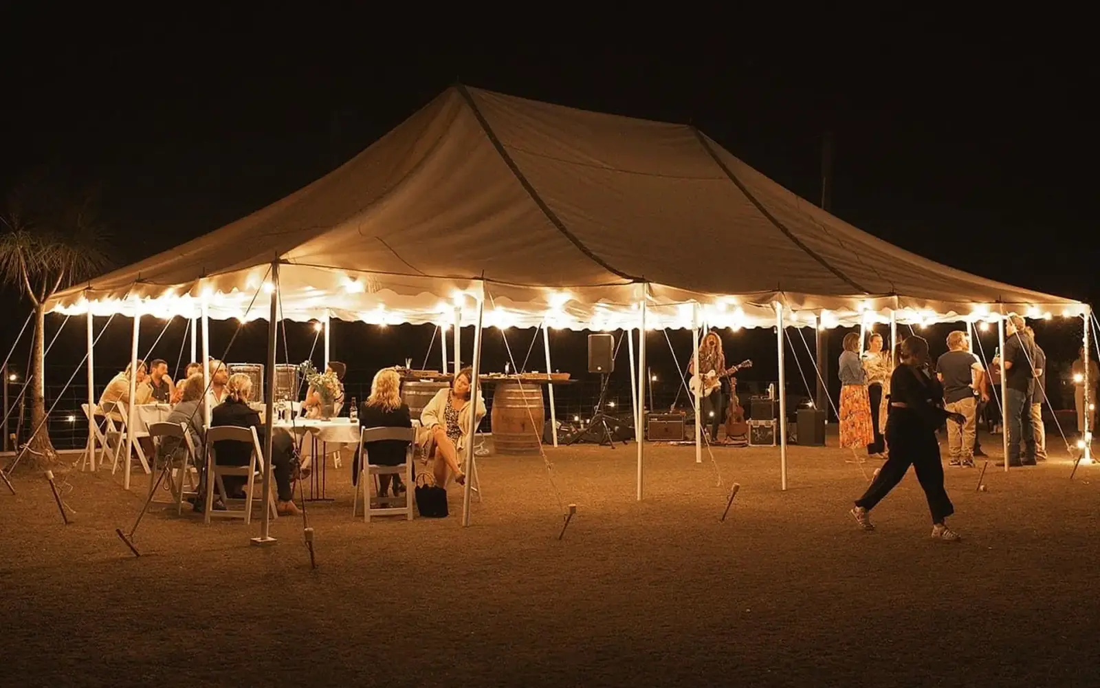 Peg-and-pole marquee at night with a musician playing to seated guests