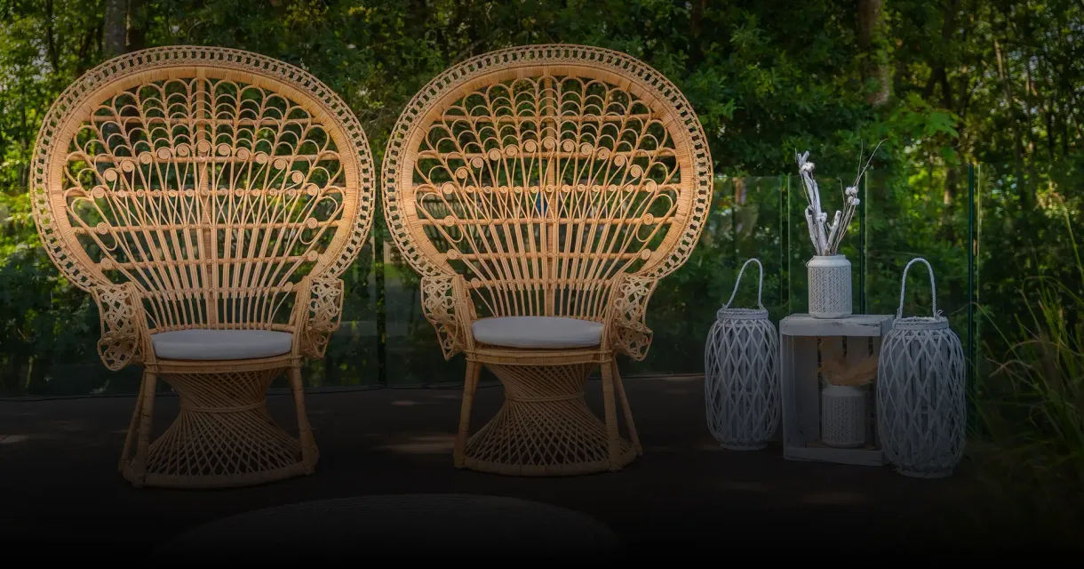 Two rattan peacock chairs with white cushions beside lanterns at an outdoor event