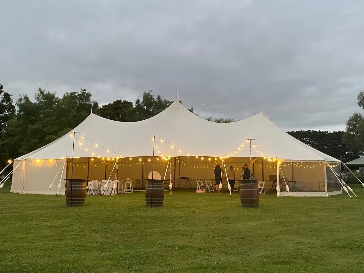 Sailcloth marquee lit with festoon lights at dusk beside wine barrels