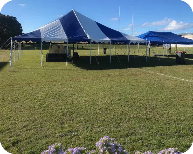 Blue and white striped peg-and-pole marquee set up on a sports oval on a sunny day